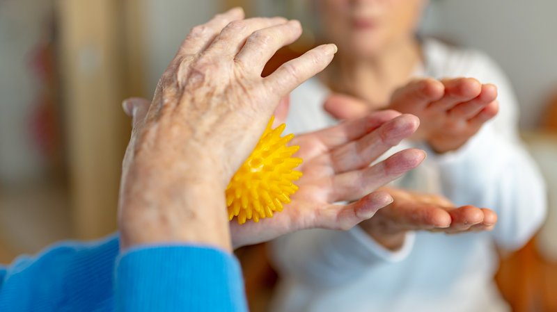 Eine ältere Dame macht Reha-Übungen mit einem Igelball